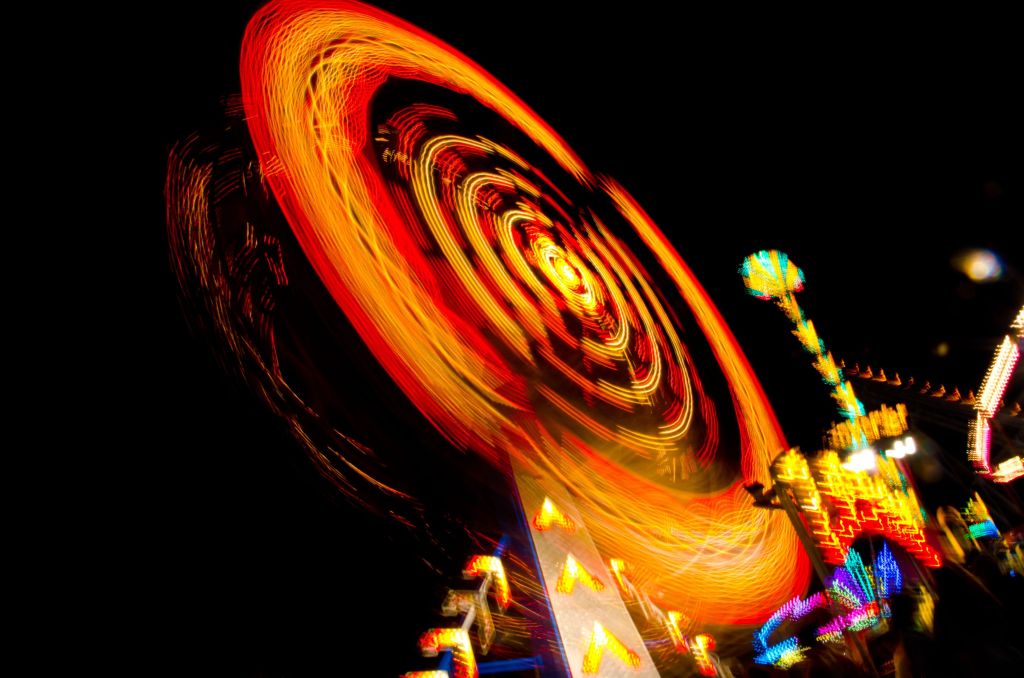 A vibrant long exposure photo captures a spinning carnival ride creating a dynamic swirl of light