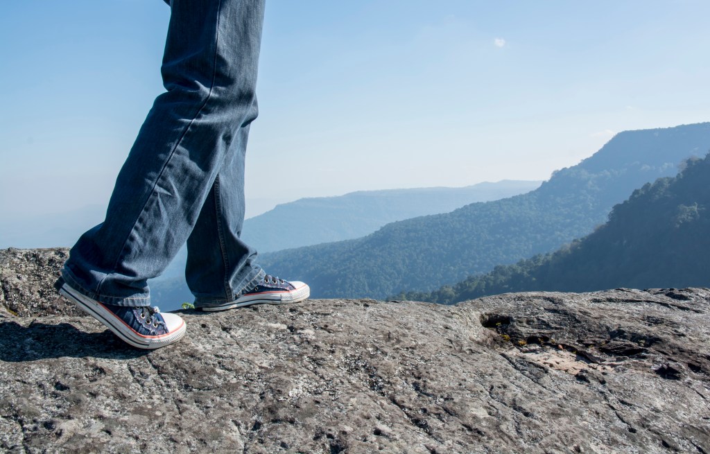 Man walking on edge of a cliff mountain top , travel concept